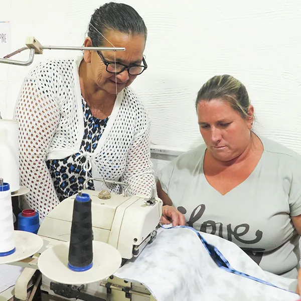 Mujeres cortando y midiendo tela sobre una mesa de trabajo durante una capacitación